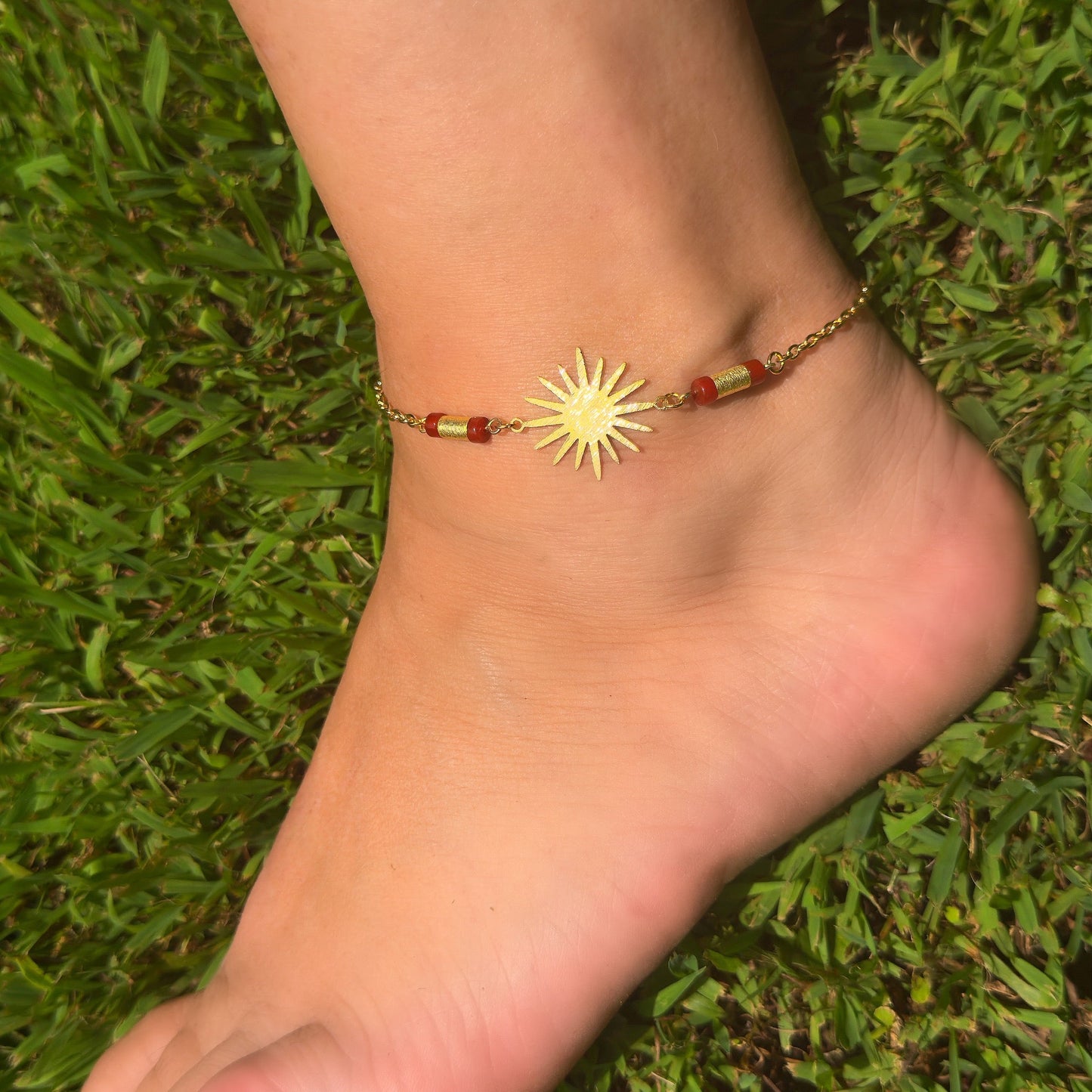 Ankle with a sun-shaped anklet on a grassy background