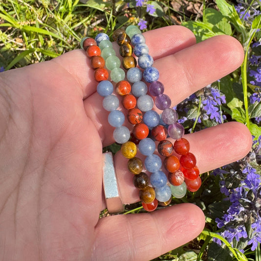 Hand holding colorful beaded bracelets with a natural background of greenery and purple flowers