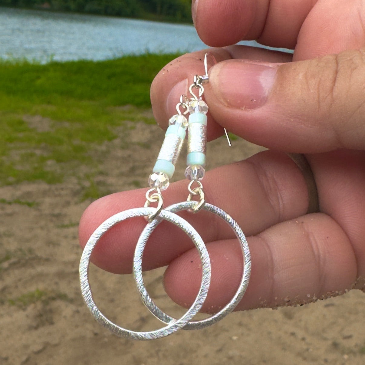 Silver hoop earrings held by a hand with a natural background